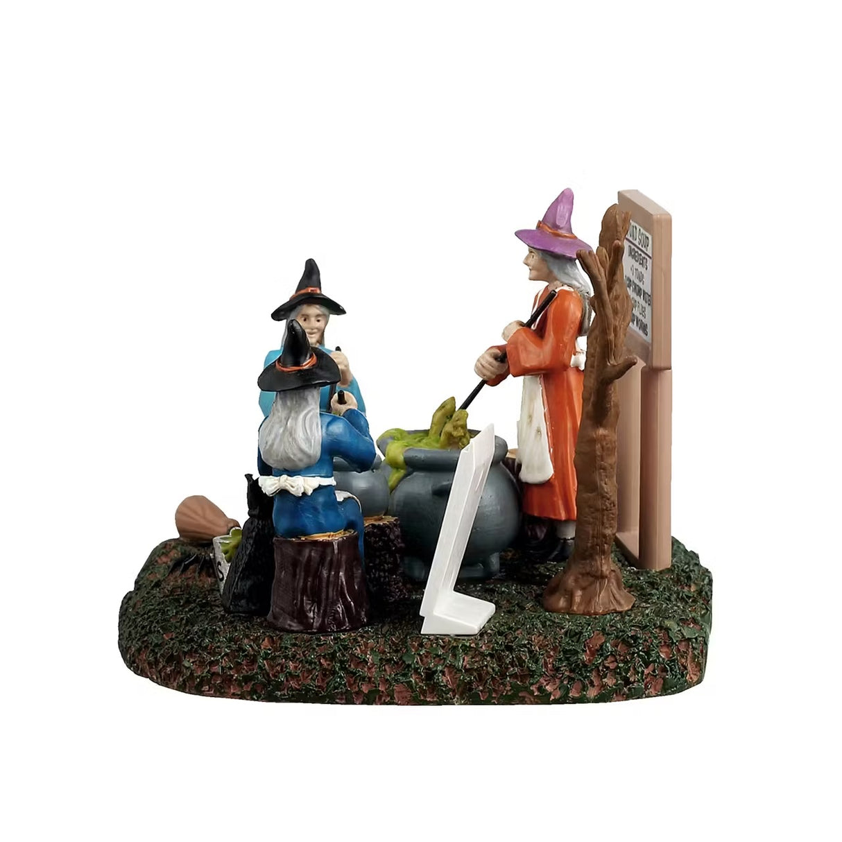 This is a different angle of the Lemax Spooky Town table accent designed to look like three witches sitting around stirring their individual cauldrons. There's a white board that reads "TOAD SOUP. Ingredients: 3 toads, 1 cup of swamp water, 1 cup of flies and 1 cup of worms." One witch is sitting on a stool and is wearing a blue cloak with a black hat. One witch is sitting on a tree stump and is wearing a dark blue cloak with a black hat. One witch is standing and is wearing an orange cloak with a pink hat.