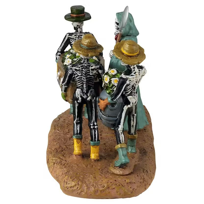 This is a different angle of the Lemax Spooky Town table accent that's designed to look like three skeletons carrying a coffin full of daisies. They're all wearing garden hats and rubber boots. There's a Grim Reaper wearing a teal cloak pointing the way.
