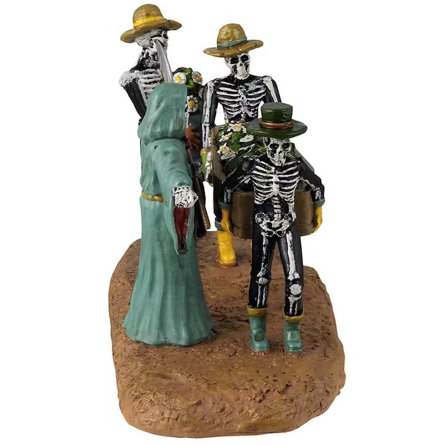 This is a different angle of the Lemax Spooky Town table accent that's designed to look like three skeletons carrying a coffin full of daisies. They're all wearing garden hats and rubber boots. There's a Grim Reaper wearing a teal cloak pointing the way.
