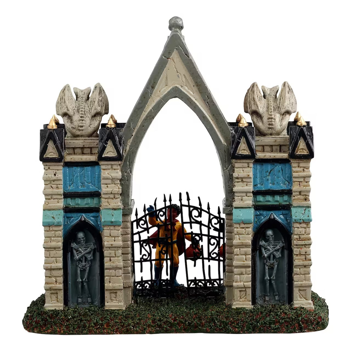 This is a different angle of the Lemax Spooky Town table accent designed to look like a Gothic gate. There are gargoyles and skeletons and pointed columns. There are also two trick or treaters trying to get in. One is dressed like a purple witch and the other is dressed like a superhero with a red cape.