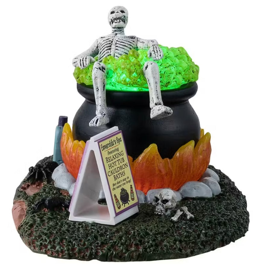 A different angle - This is a Lemax Spooky Town table accent designed to look like a skeleton taking a bath in a big, black cauldron. The water glows green. There's a stool with a towel and a spider on it. Next to the cauldron, there's a tube of Spa Bath Soap. There's a sign next to the cauldron that reads "Esmeralda's Spa featuring Relaxing Hot Tub Cauldron Baths. But don't stay in the water too long!"