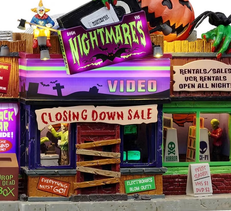 This is an up close view of the building. On the roof, there's a creepy clown holding an axe and a giant jack-o-lantern with green hands holding a giant VHS tape and a tarantula. You can see inside the building there are people shopping and looking through the shelves.