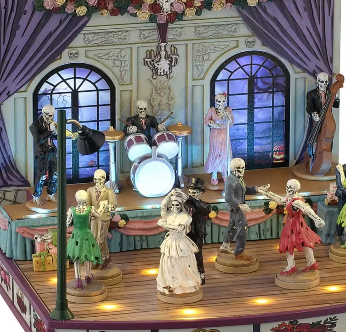 This is an up close view of the wedding hall. There's a band on the stage: a trumpeter, a drummer, a singer and a cello. The bride and groom are dancing among other skeletal guests.