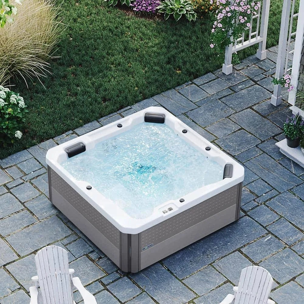 This is a lifestyle picture of this filled hot tub from above. It's on a brick patio next to two adirondack chairs.