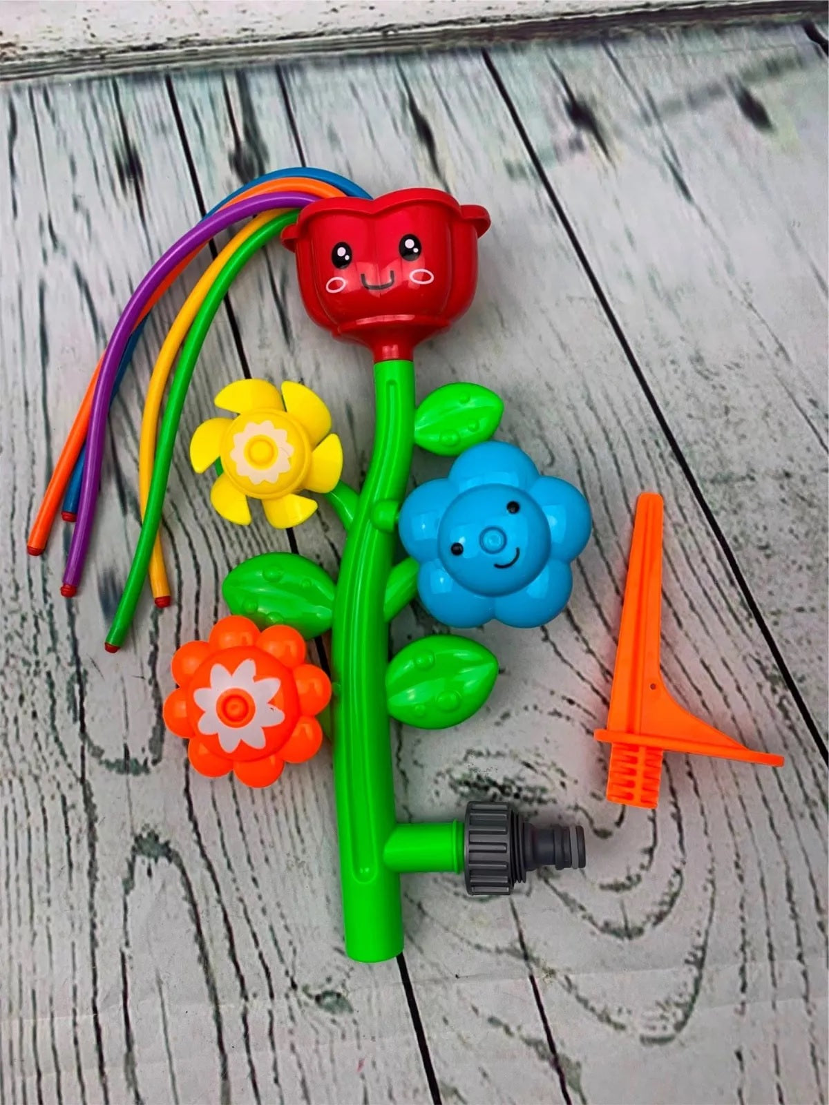 Sprinkler shaped like a stem with four "petals." The top flower has five wiggly hoses coming out of it. The other flowers spin to shoot the water in different directions. The flower colors in this image are red, orange, yellow and blue.