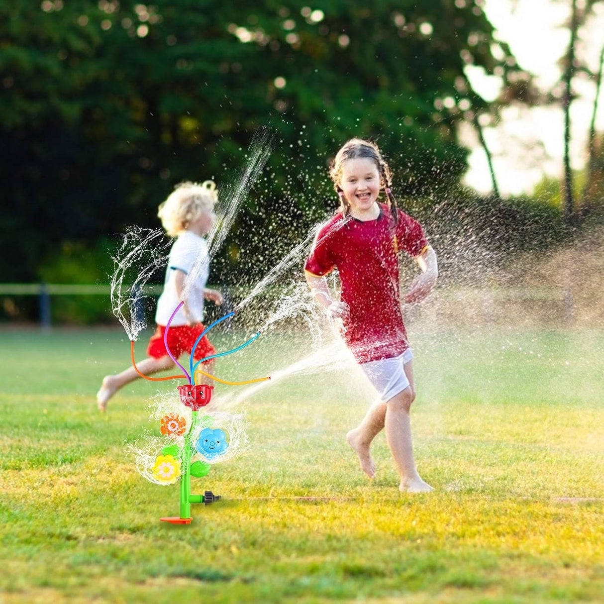 Sprinkler shaped like a stem with four "petals." The top flower has five wiggly hoses coming out of it. The other flowers spin to shoot the water in different directions. This is a lifestyle image showing two kids playing in the sprinkler's water.