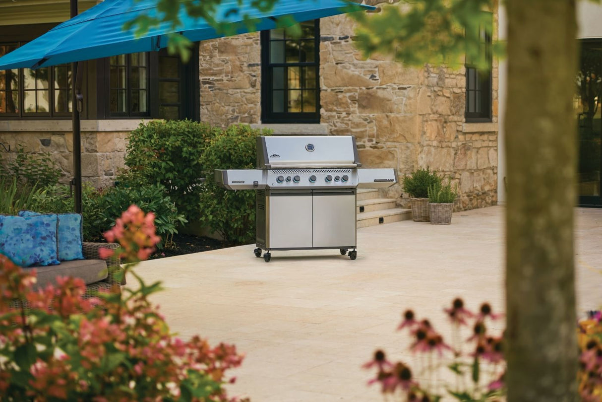 This is a lifestyle image showing off this specific grill on an outdoor patio underneath a blue cantilever umbrella.