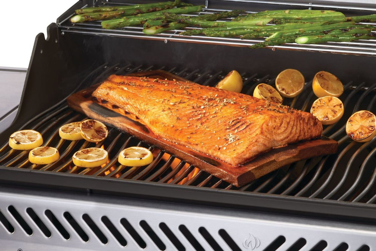 This is an up close view of the grill in use. There's asparagus cooking on the top shelf and fish with lemons cooking on the bottom shelf. The fish is cooking on a wooden plank.