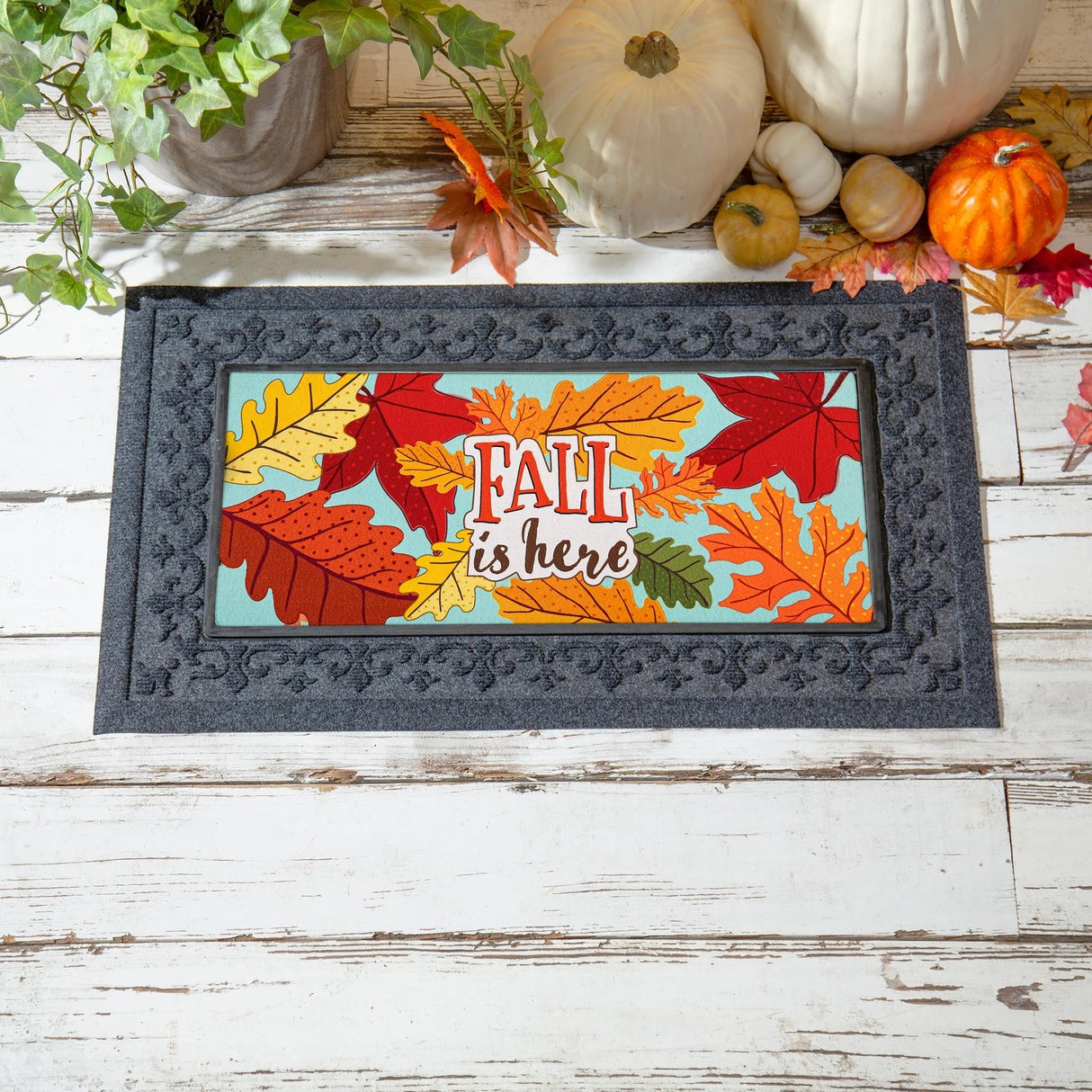 Light blue welcome mat that reads "Fall is here." There are yellow, orange, red and green leaves.