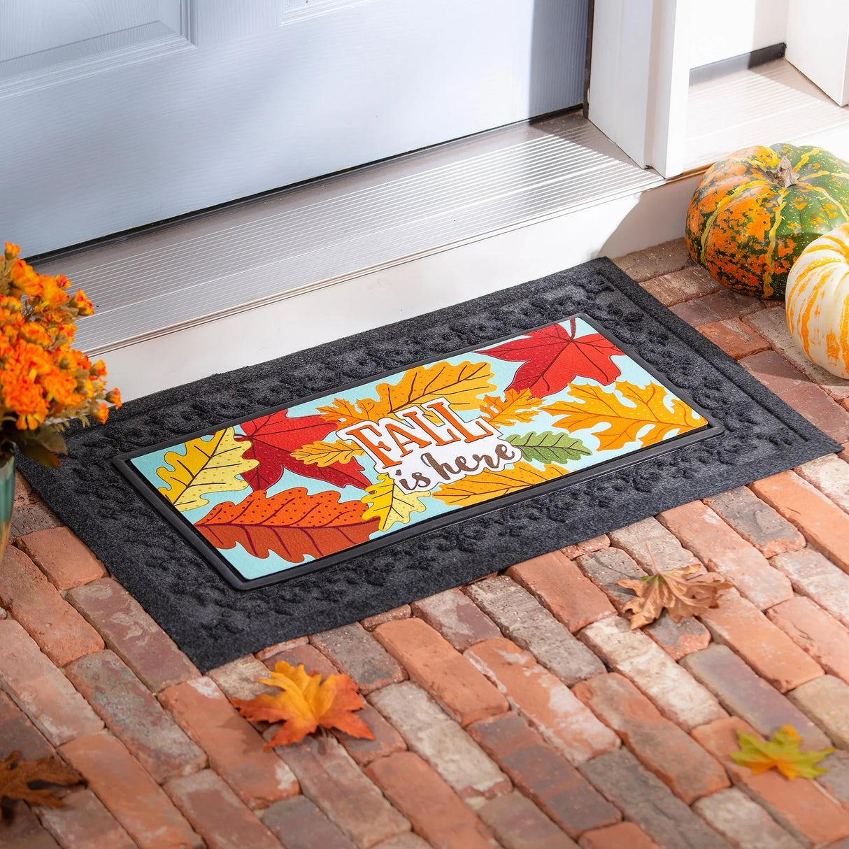 Light blue welcome mat that reads "Fall is here." There are yellow, orange, red and green leaves.