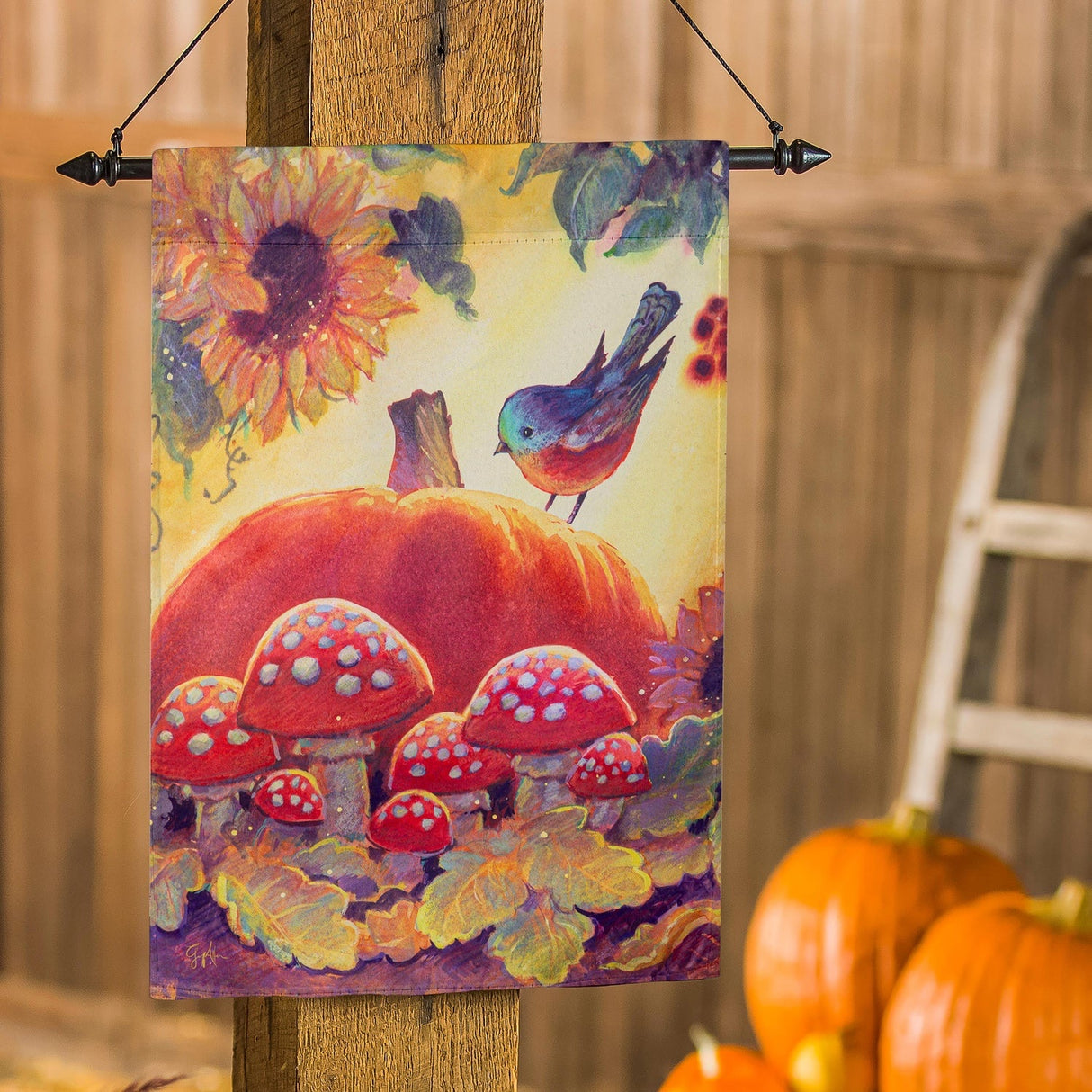 Yellow flag that features a sunflower, leaves, mushrooms, a large pumpkin and a blue bird sitting on the pumpkin.