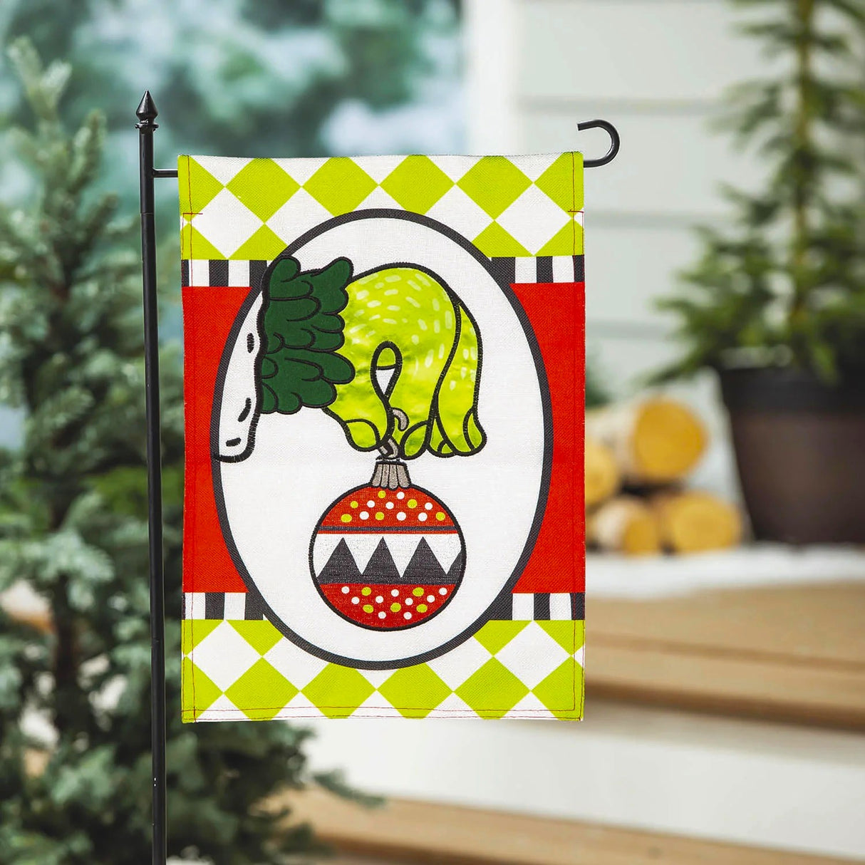 Flag with a cartoon depiction of The Grinch's green hand holding an ornament. There are also lime green diamonds, a black and white stripe and red designs.