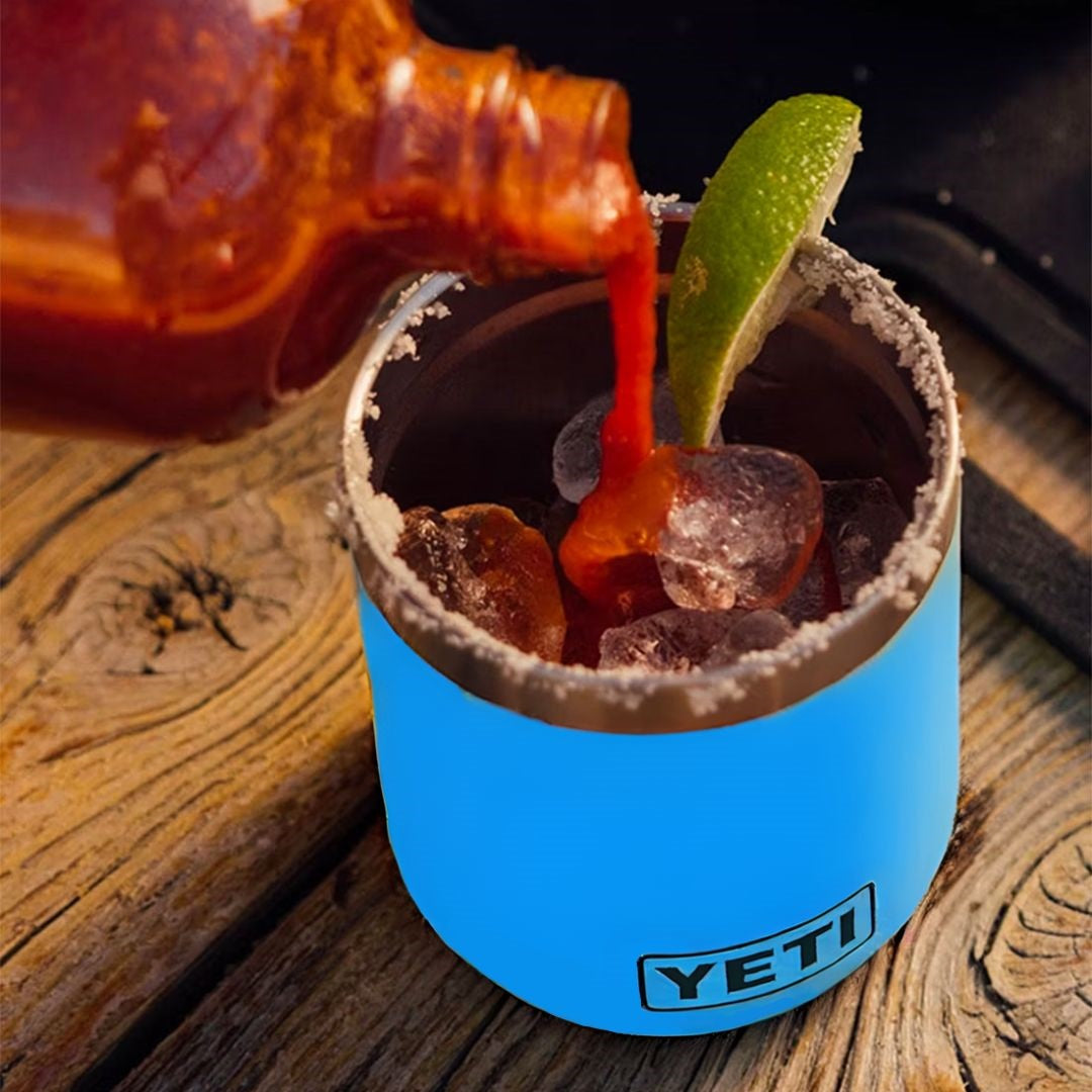 Blue colored lowball Yeti cup. This is a lifestyle image showing someone making a Bloody Mary drink inside of the cup.