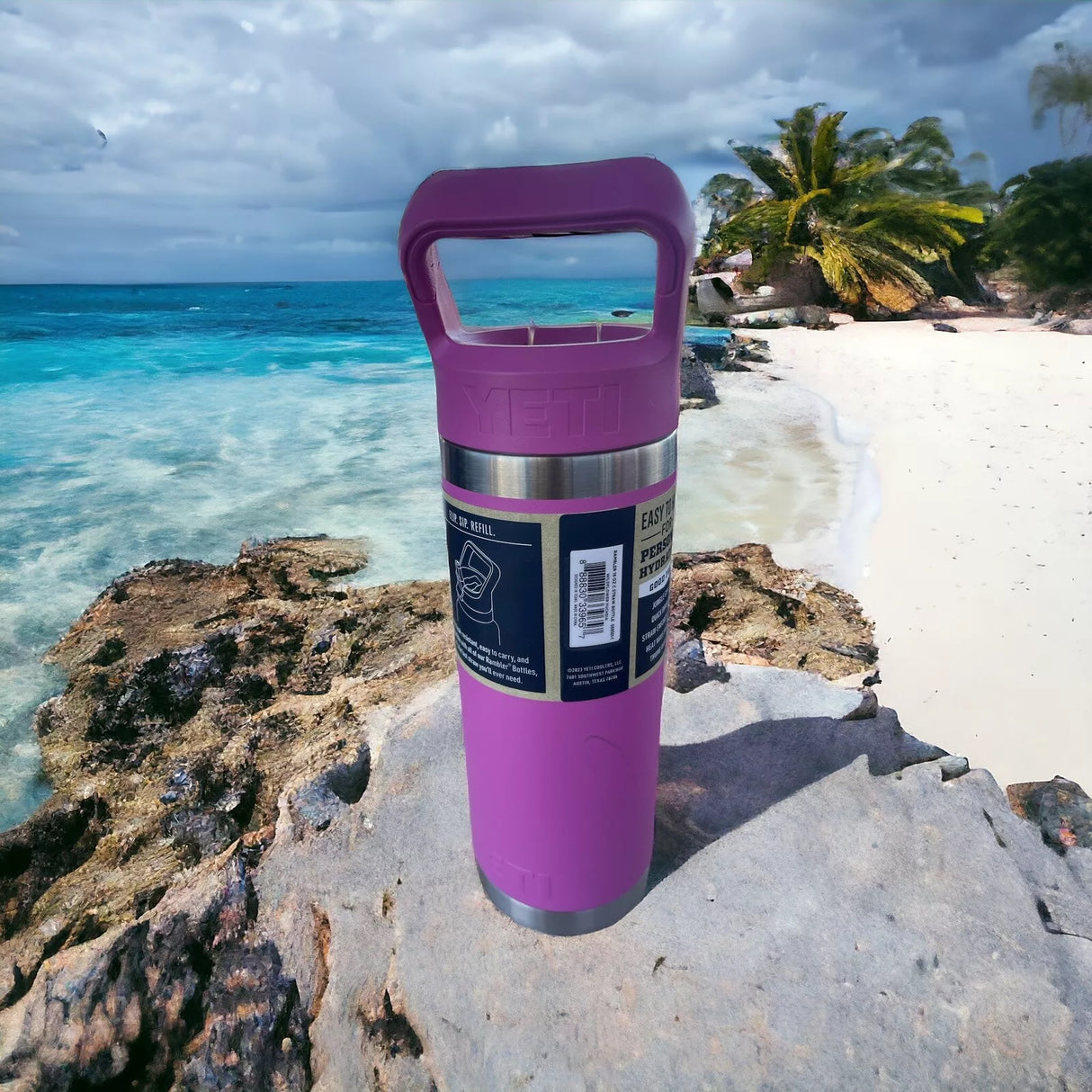 Fuchsia colored 18 oz. YETI water bottle. This lifestyle image shows it on a rock with an ocean and a beach in the background.