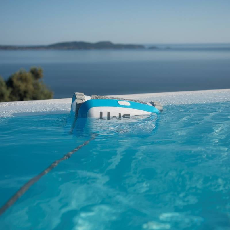 Robotic pool cleaner. Body is blue and white with gray bristles. This image shows the Cosmy vacuum going into the water of a pool.