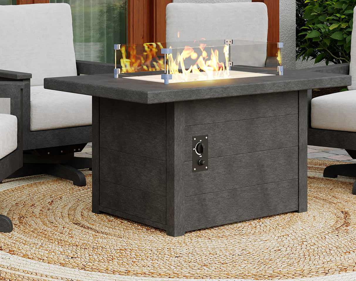 A rectangular black resin fire pit table on an outdoor carpet between a few chairs