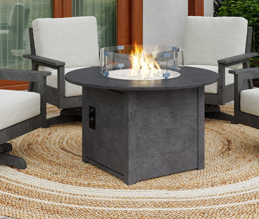 A round black resin fire pit table on an outdoor carpet between a few chairs