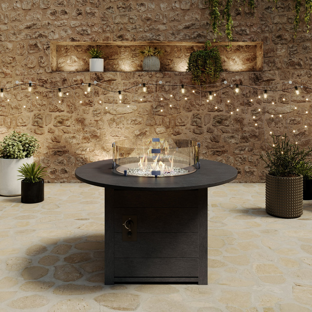 A round black resin fire pit table on a stone patio surrounded by plants