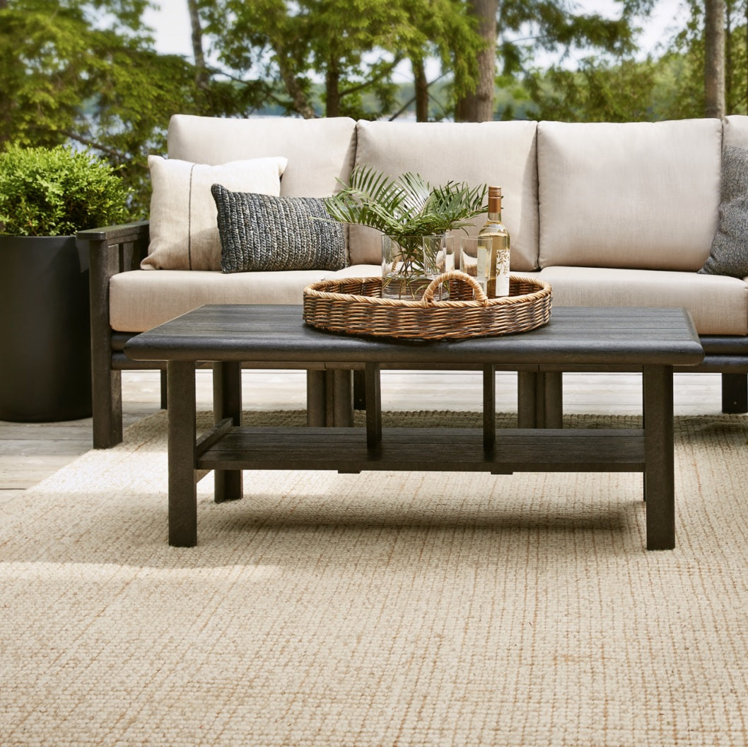 A brown resin couch with tan cushions and a brown resin coffee table on an outdoor patio with a tan rug