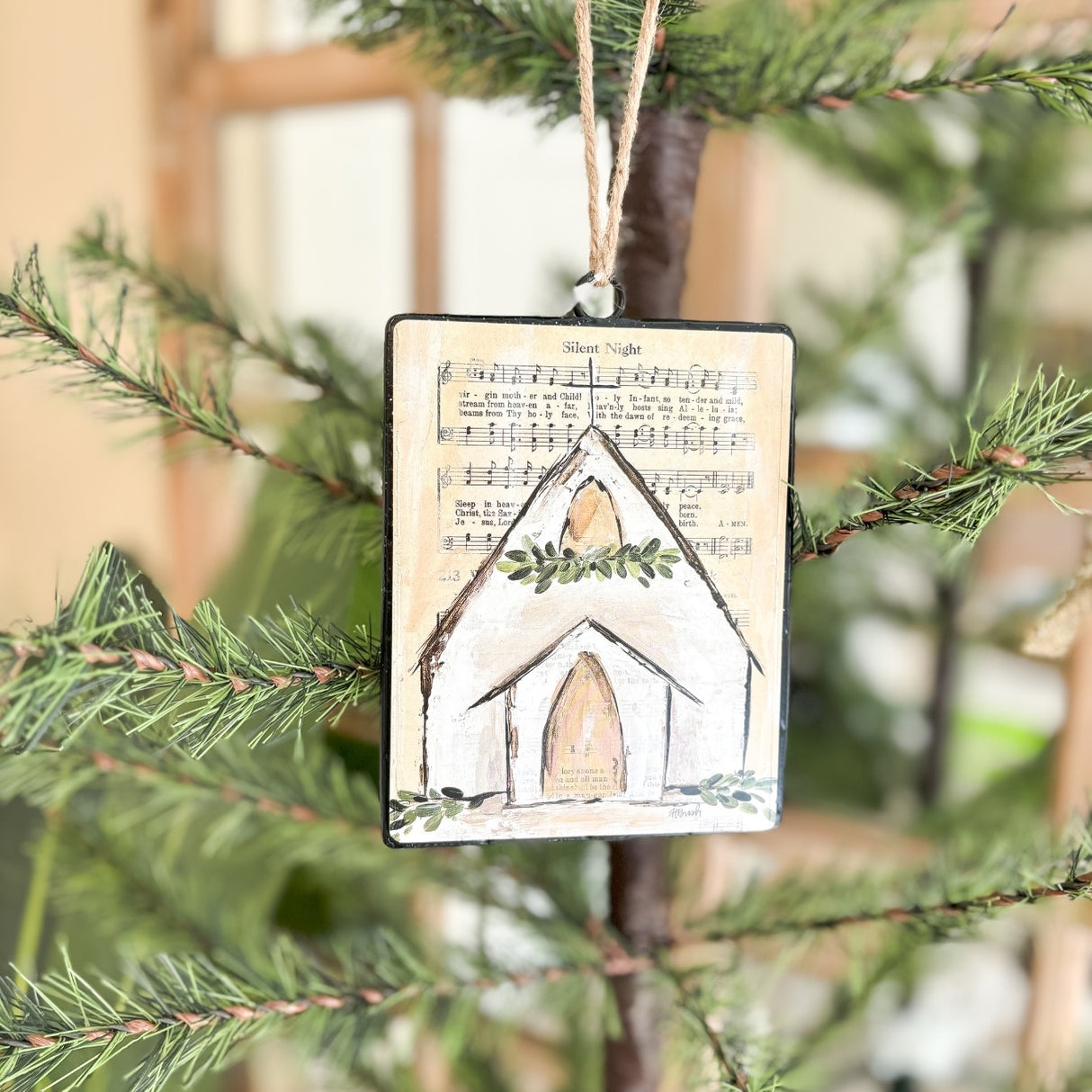 Each ornament features a background printed with sheet music; there are two options. One ornament has the sheet music for "Oh Holy Night" and a chapel with a garland at the steeple. One ornament has the sheet music for "Silent Night" and a chapel with a wreath at the steeple.