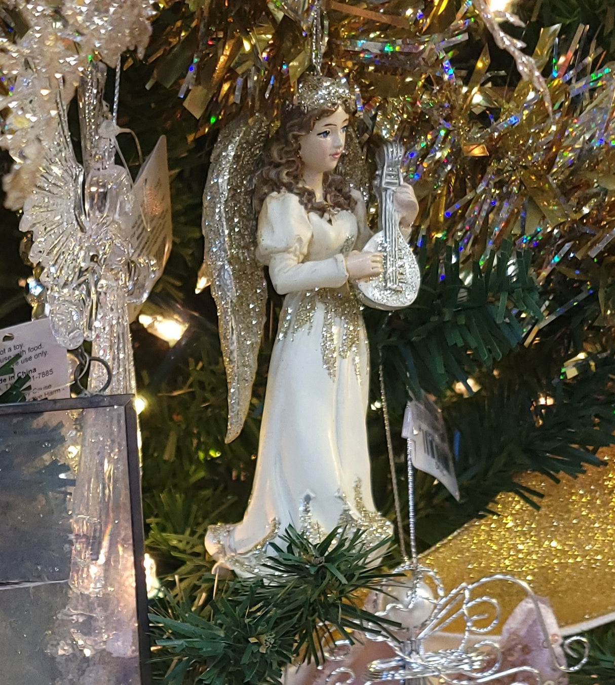 Ornament shaped like an angel holding a musical instrument. One angel is blond and holding a harp. One angel is brunette and holding a trumpet. One angel is a redhead and holding a mandolin.
