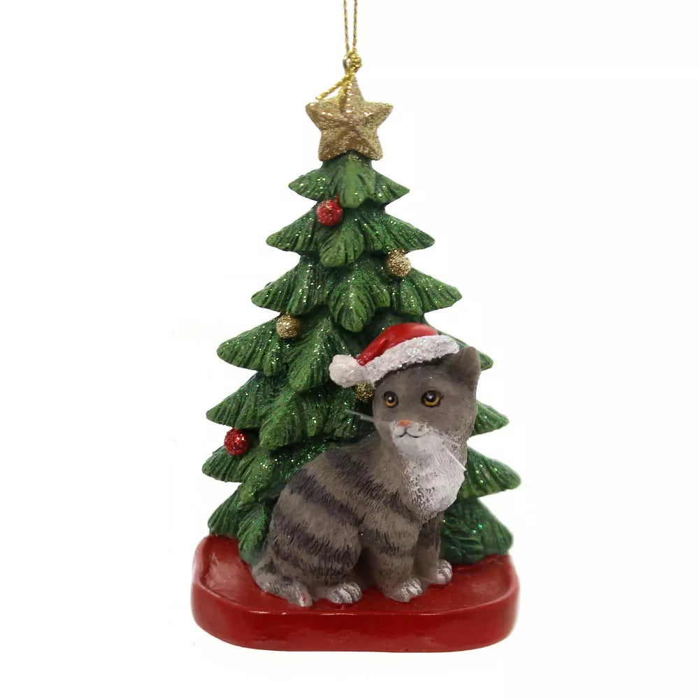 Ornaments shaped like a cat in front of a tree. One ornament features a black and white cat. One ornament features an orange and white cat. One ornament features a light gray and dark gray cat. One ornament features a white cat. All the cats are wearing Santa hats.