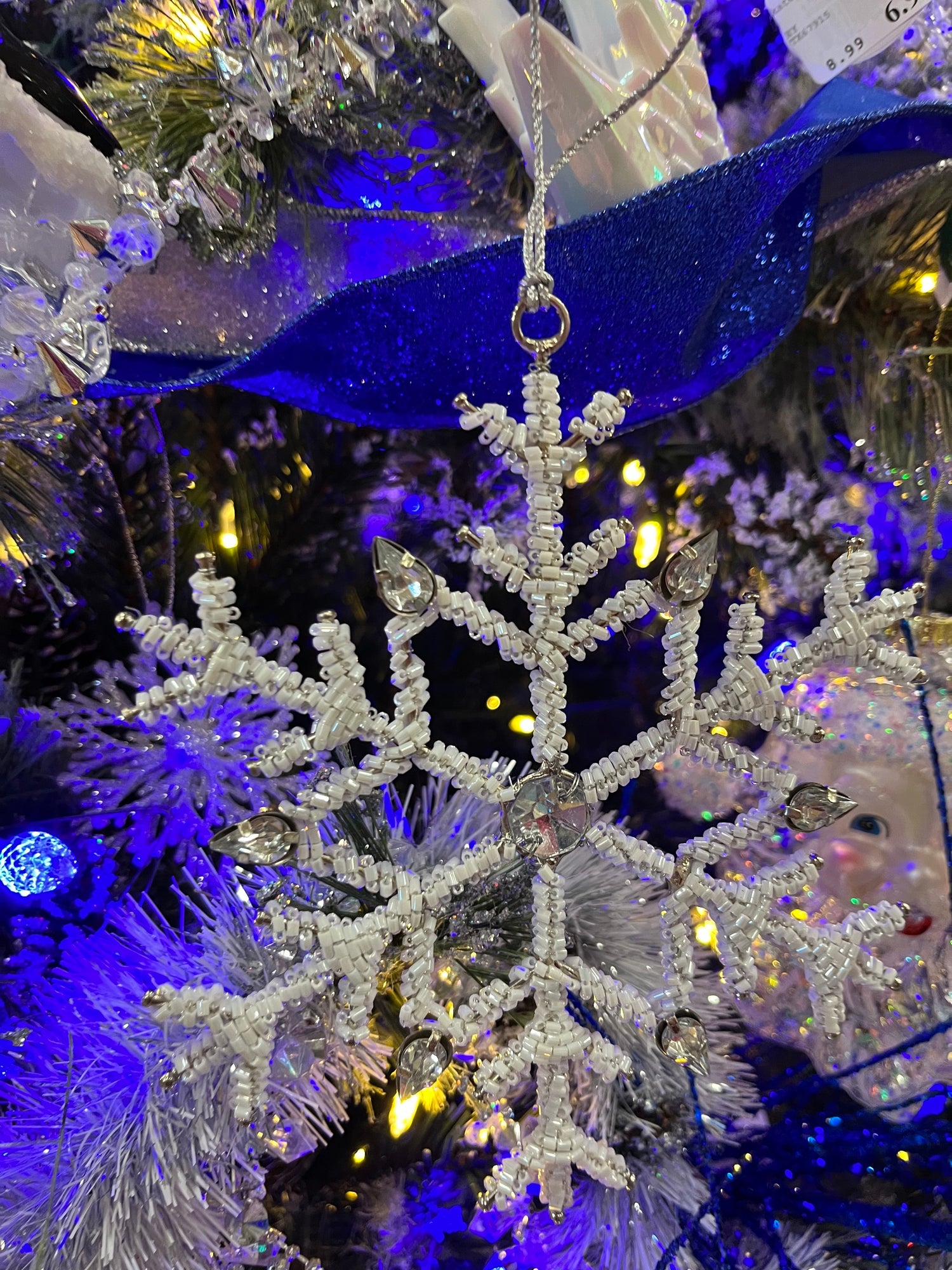 Ornament shaped like a snowflake and decorated with white beads and silver jewel accents.