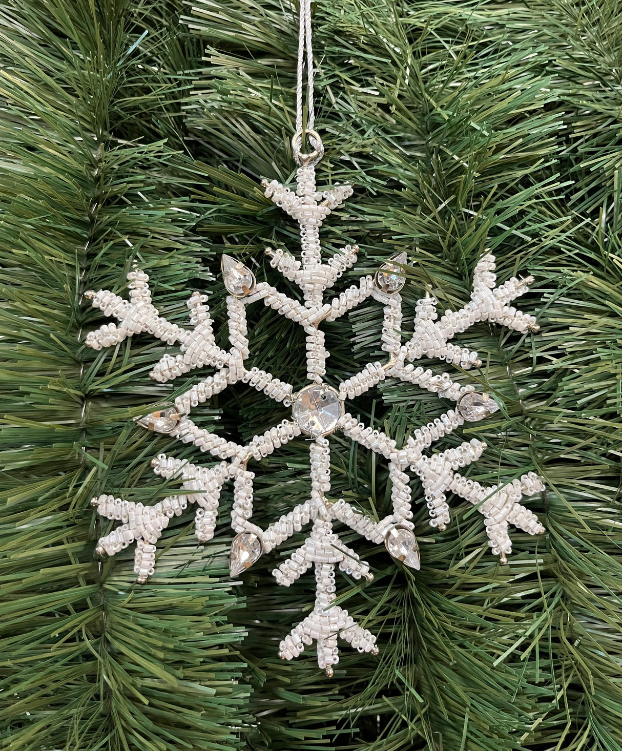 Ornament shaped like a snowflake and decorated with white beads and silver jewel accents.