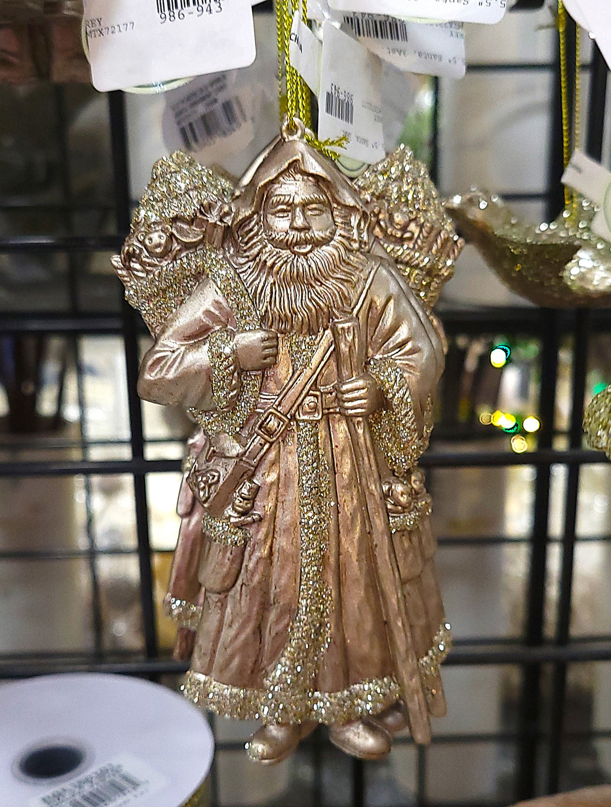 Holiday ornament shaped like an Old World Santa Claus. It's made of gold plastic to look vintage. One Santa is holding a staff and one Santa is holding a bell.