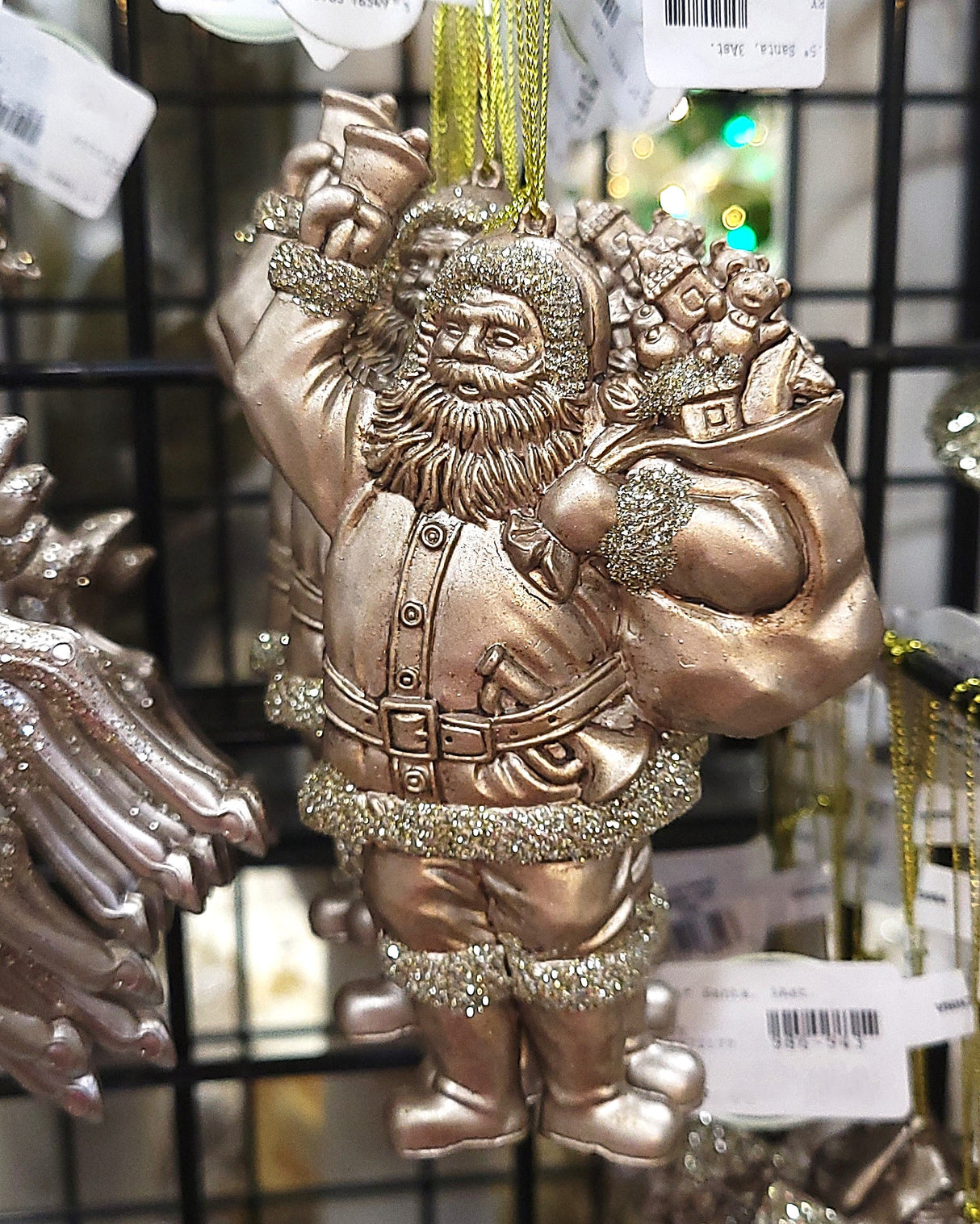 Holiday ornament shaped like an Old World Santa Claus. It's made of gold plastic to look vintage. One Santa is holding a staff and one Santa is holding a bell.