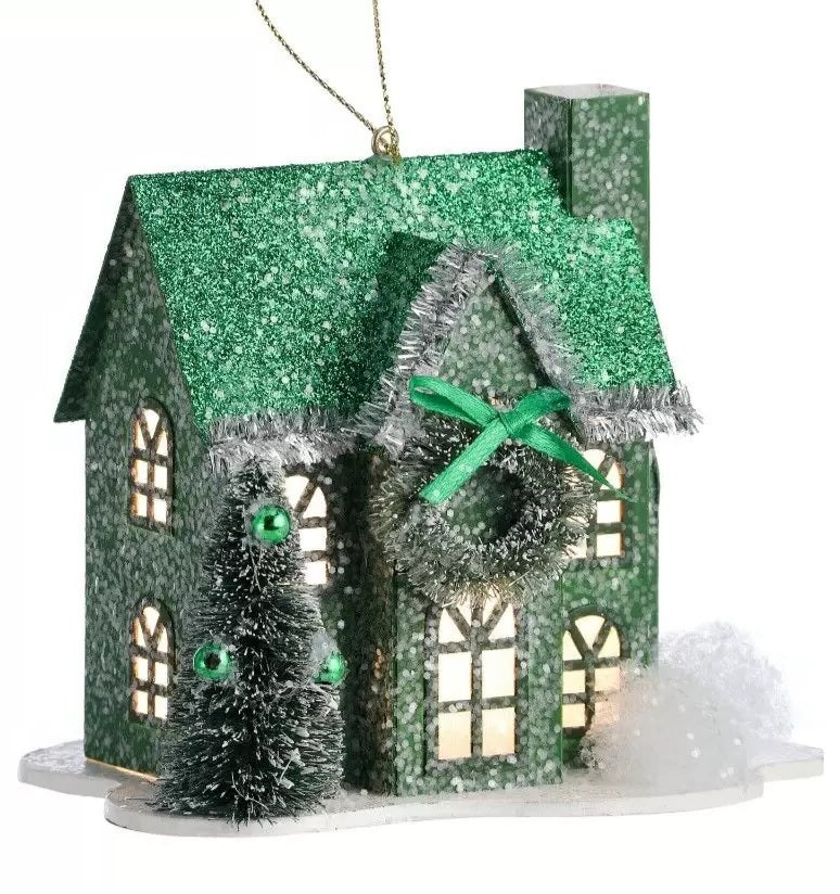 Ornament shaped like a house covered in snow. One house is red and features a wreath near the roof with a red bow. One house is green and features a wreath near the roof with a green bow.