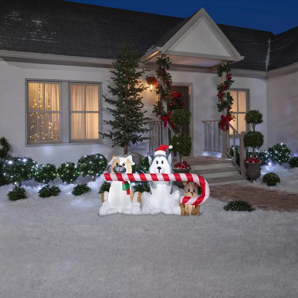 Christmas inflatable shaped like three dogs holding a giant candy cane in their mouths. One dog is wearing a red and green sweater. Another dog is wearing a Santa hat.