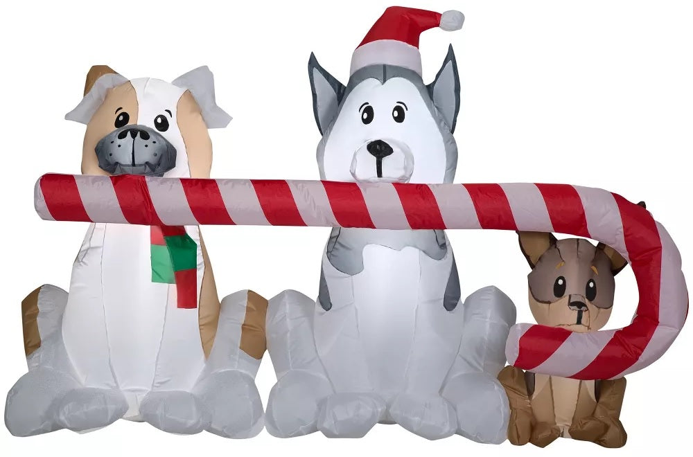 Christmas inflatable shaped like three dogs holding a giant candy cane in their mouths. One dog is wearing a red and green sweater. Another dog is wearing a Santa hat.