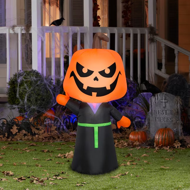 This image shows the Pumpkin Head Reaper Inflatable in front of a house decorated for Halloween. The head has two eyes, a nose and a mouth with three teeth. He's wearing a black robe with a lime green belt.