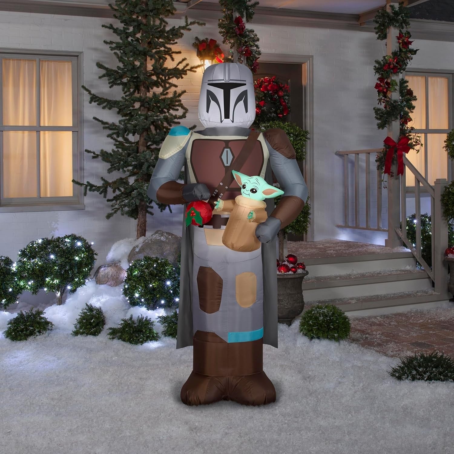 Christmas inflatable designed to look like the Star Wars characters The Mandalorian and Grogu. Mando is holding Grogu and a red holiday ornament.