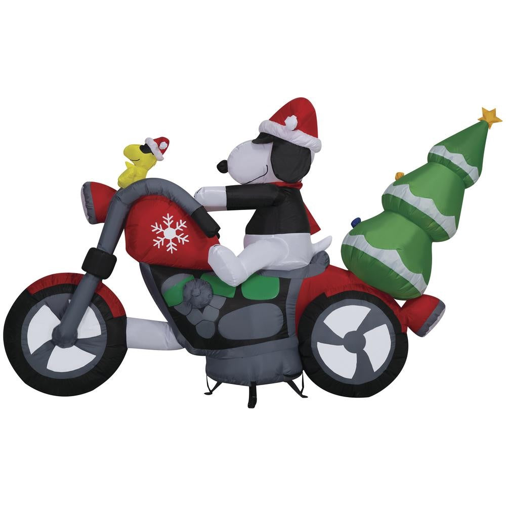 Christmas inflatable. It features Snoopy wearing a Santa hat and wearing sunglasses. Snoopy is driving a red motorcycle with a snowflake accent on it. There's a decorated Christmas tree on the back and Woodstock is riding on the handlebars. There are LED lights inside.