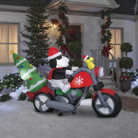 Christmas inflatable. It features Snoopy wearing a Santa hat and wearing sunglasses. Snoopy is driving a red motorcycle with a snowflake accent on it. There's a decorated Christmas tree on the back and Woodstock is riding on the handlebars. There are LED lights inside.