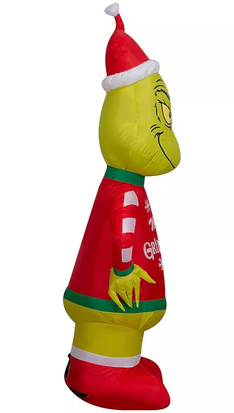 Christmas inflatable shaped like the cartoon character The Grinch. The Grinch is wearing a Santa hat and an "ugly" sweater that reads "Merry Grinchmas." The sleeves on the sweater are red and white striped.