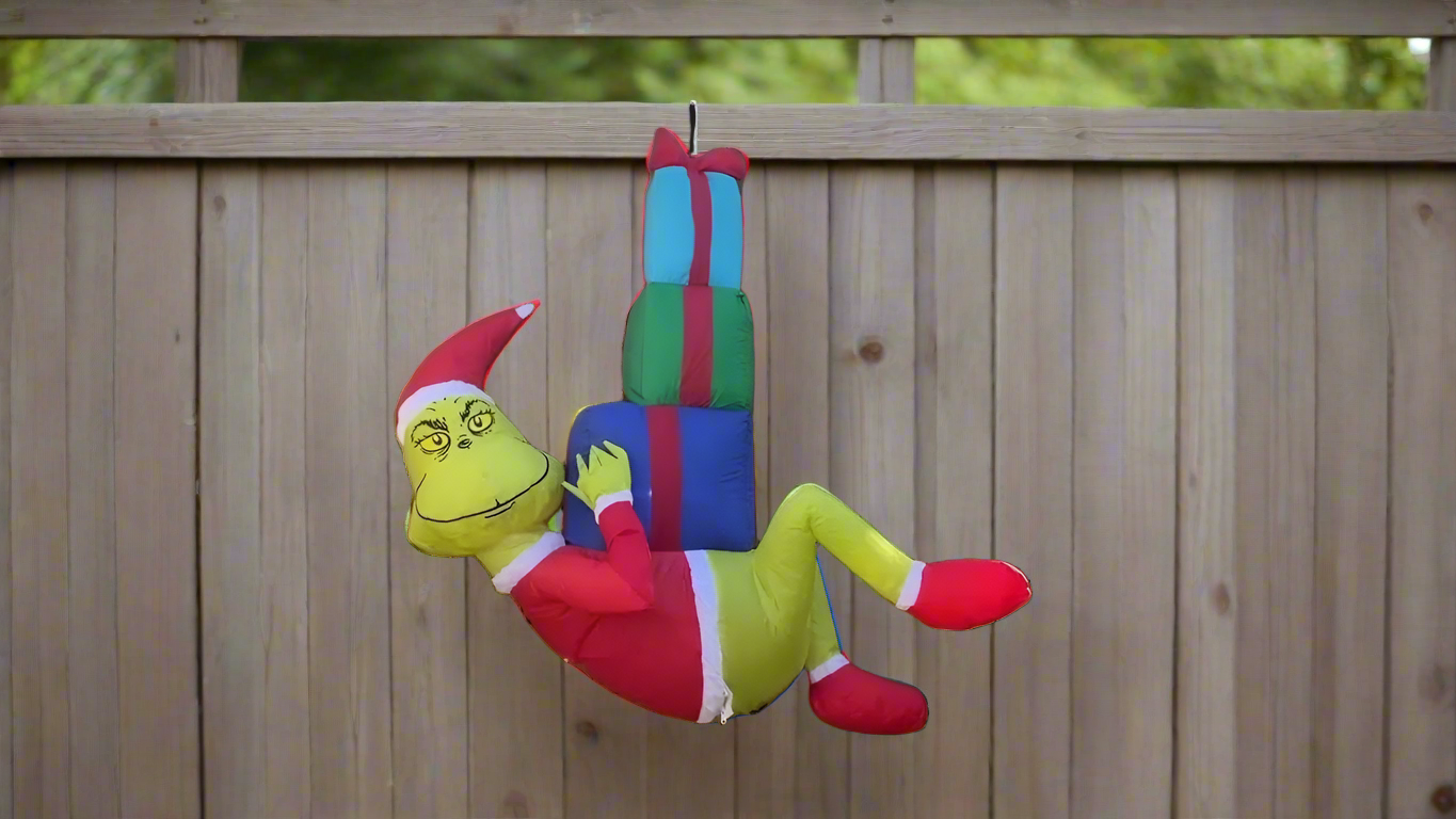 Christmas inflatable designed to look like The Grinch dressed as Santa and hanging from a rope, holding presents.