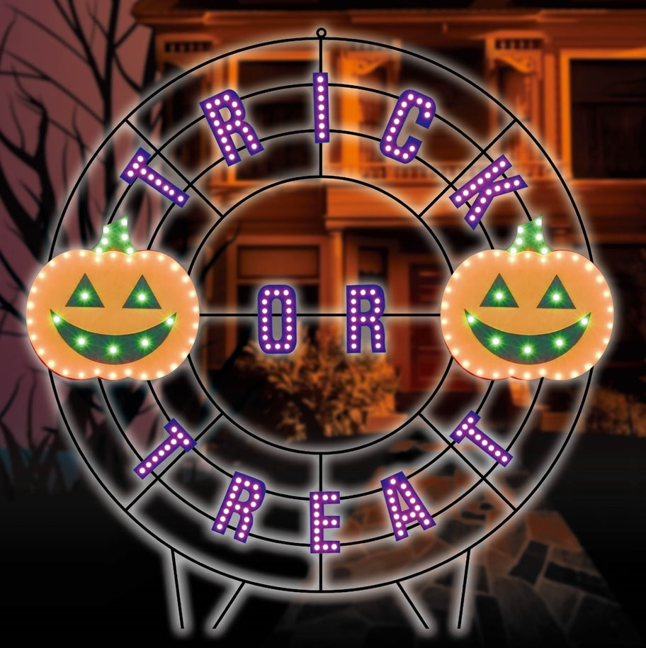 A black wire frame wreath with purple words that read "TRICK OR TREAT." There are two orange jack-o-lanterns with green eyes and mouths.