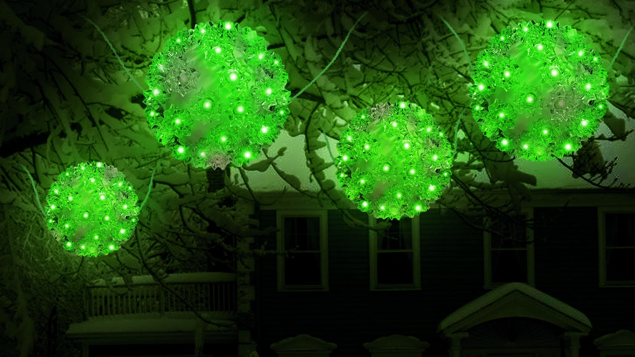 Outdoor lights hanging from snow covered tree branches. The lights are spheres and lit with green lights.