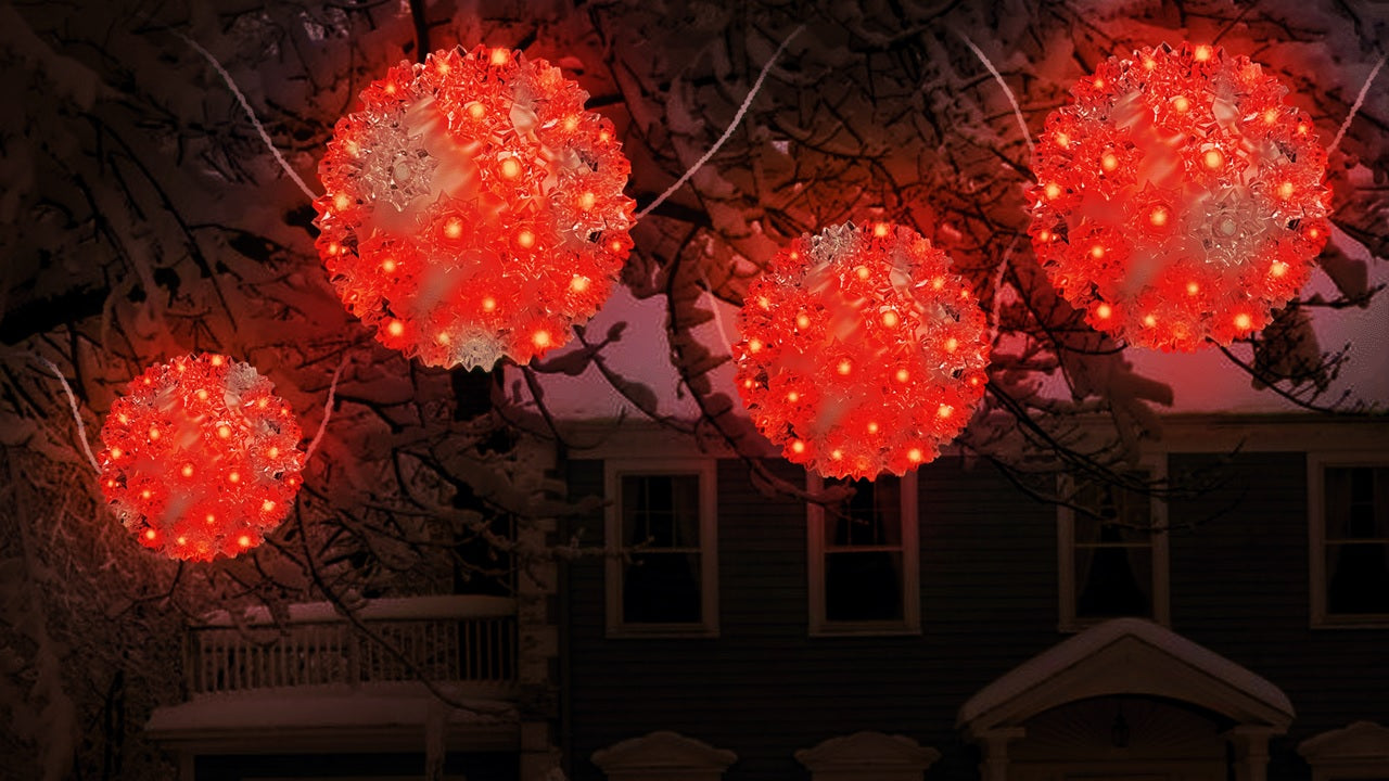 Outdoor lights hanging from snow covered tree branches. The lights are spheres and lit with red lights.