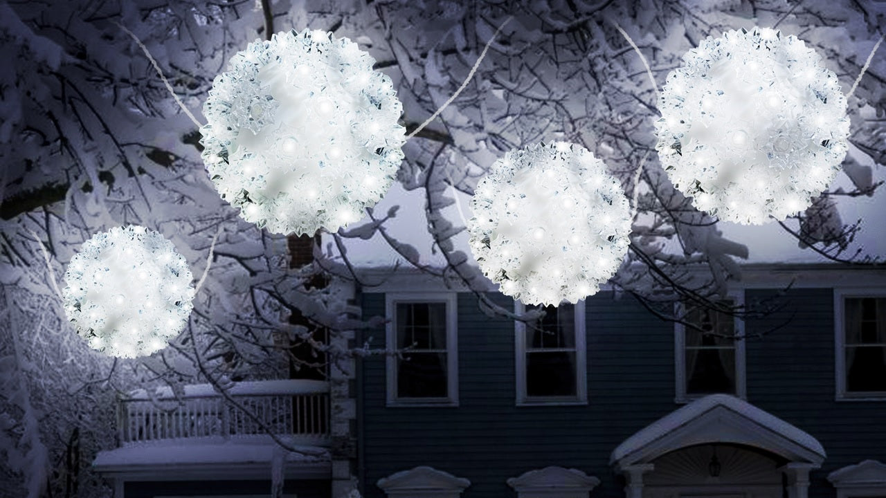Outdoor lights hanging from snow covered tree branches. The lights are spheres and lit with pure white lights.