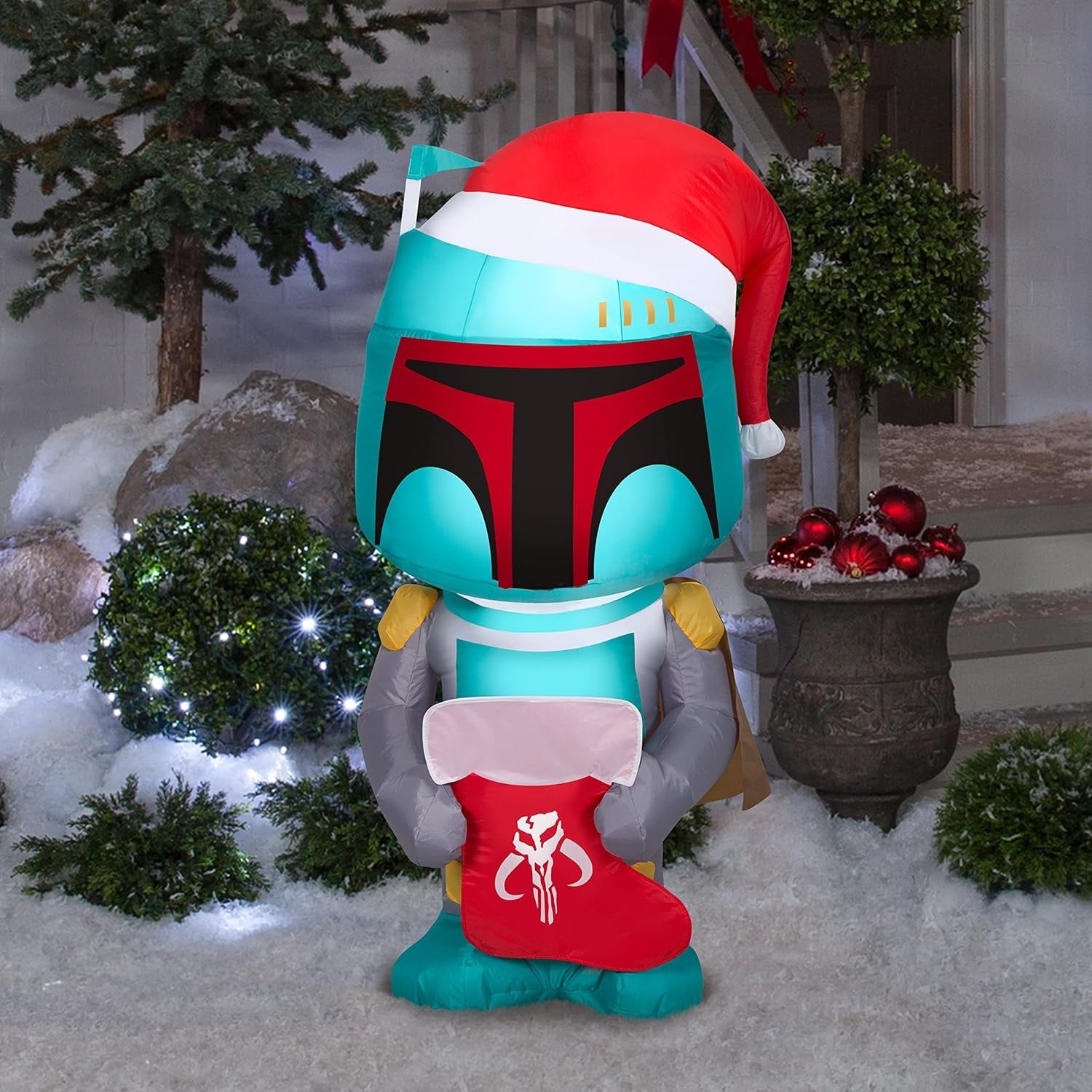 Christmas inflatable designed to look like the famous Star Wars character Boba Fett. He's wearing a Santa hat and holding a stocking with the Mandalorian symbol on it.