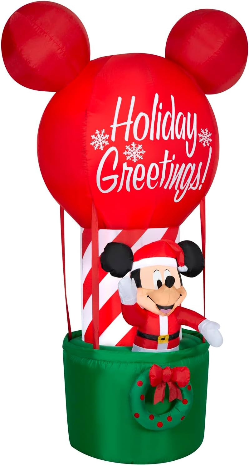 Christmas inflatable shaped like Mickey Mouse dressed as Santa and standing in a hot air balloon basket. The basket is green with a green wreath on it. The balloon is shaped like Mickey's head and ears. The balloon reads "Holiday Greetings!"