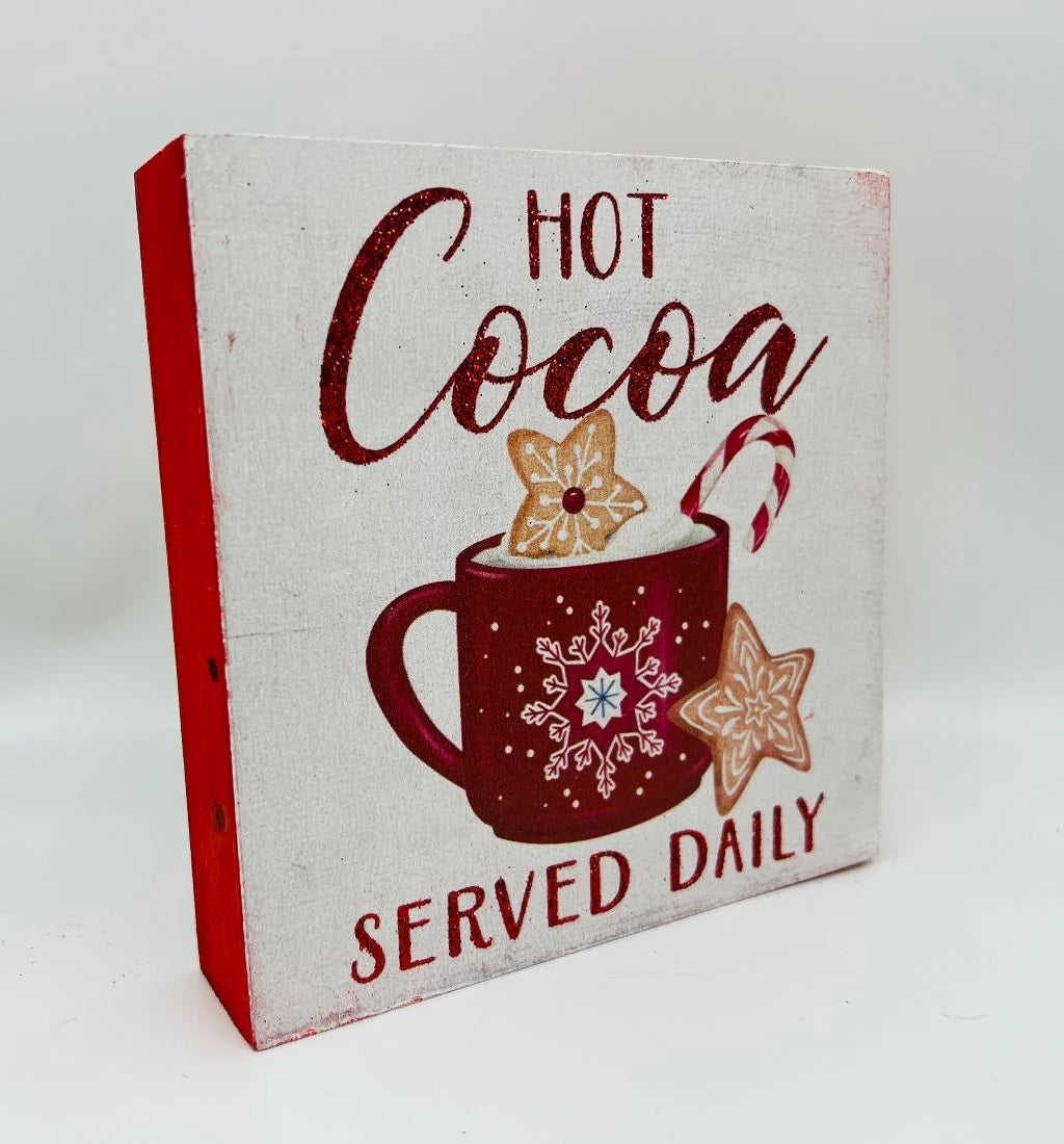 One sign features two gingerbread people outside of a gingerbread house and reads "Home Sweet Home." One sign reads "Joy to the World" and has some gingerbread cookie accents. One sign reads "Hot Cocoa Served Daily" and features a mug with cookies and a candy cane inside. One sign reads "Sip and Enjoy" and features two mugs with different designs.