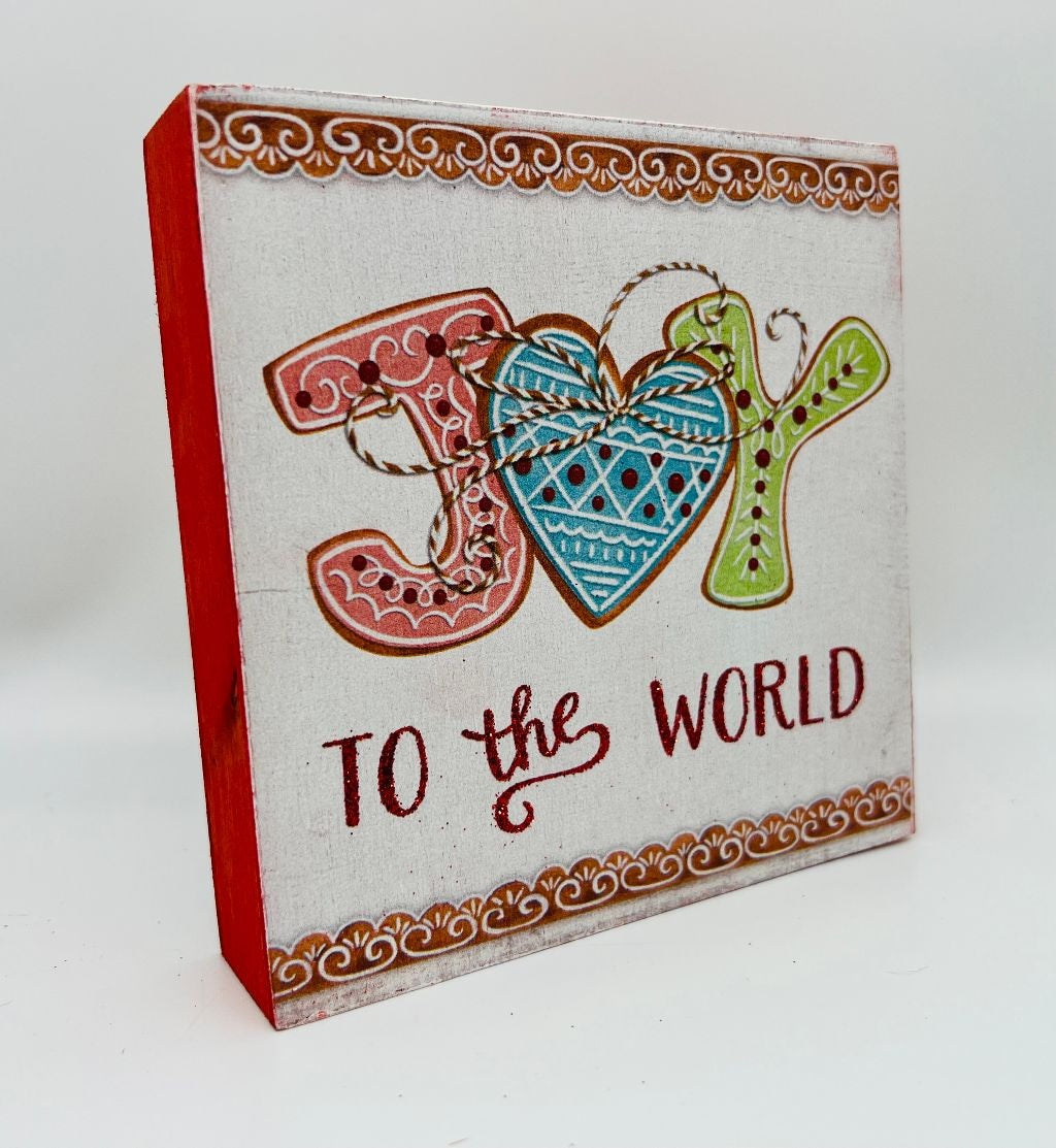 One sign features two gingerbread people outside of a gingerbread house and reads "Home Sweet Home." One sign reads "Joy to the World" and has some gingerbread cookie accents. One sign reads "Hot Cocoa Served Daily" and features a mug with cookies and a candy cane inside. One sign reads "Sip and Enjoy" and features two mugs with different designs.