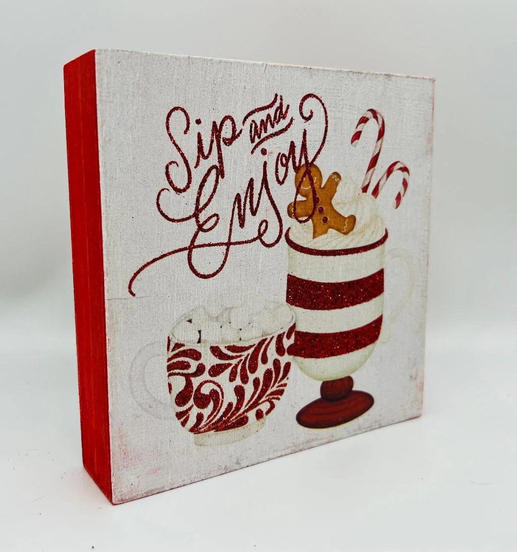 One sign features two gingerbread people outside of a gingerbread house and reads "Home Sweet Home." One sign reads "Joy to the World" and has some gingerbread cookie accents. One sign reads "Hot Cocoa Served Daily" and features a mug with cookies and a candy cane inside. One sign reads "Sip and Enjoy" and features two mugs with different designs.