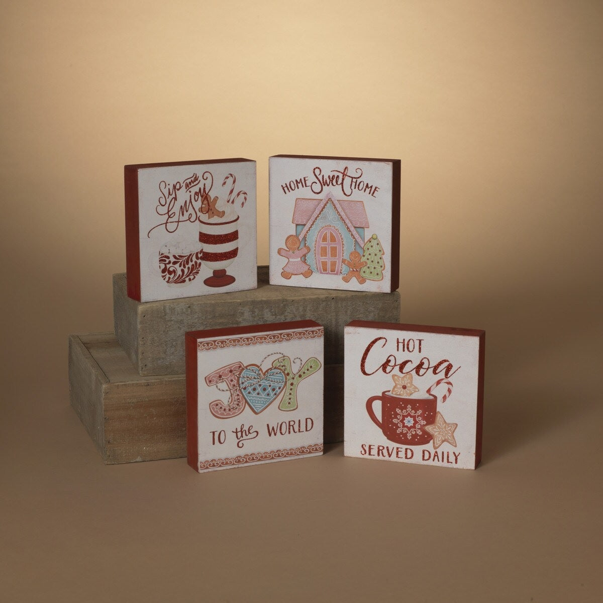 One sign features two gingerbread people outside of a gingerbread house and reads "Home Sweet Home." One sign reads "Joy to the World" and has some gingerbread cookie accents. One sign reads "Hot Cocoa Served Daily" and features a mug with cookies and a candy cane inside. One sign reads "Sip and Enjoy" and features two mugs with different designs.