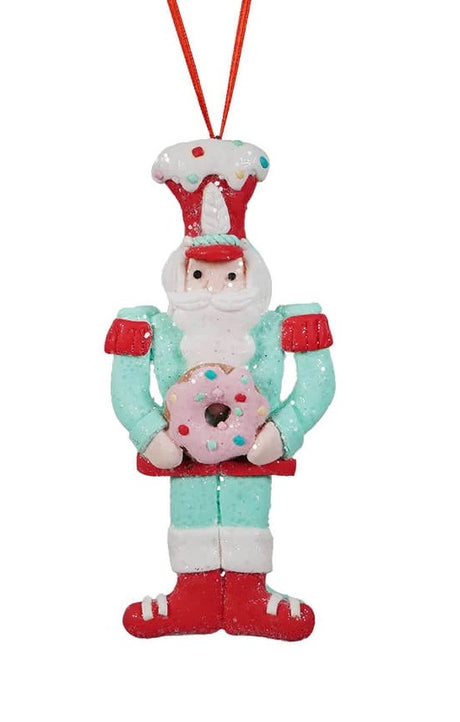 This ornament features a toy soldier wearing a light blue outfit, a red hat and he's holding a pink donut.